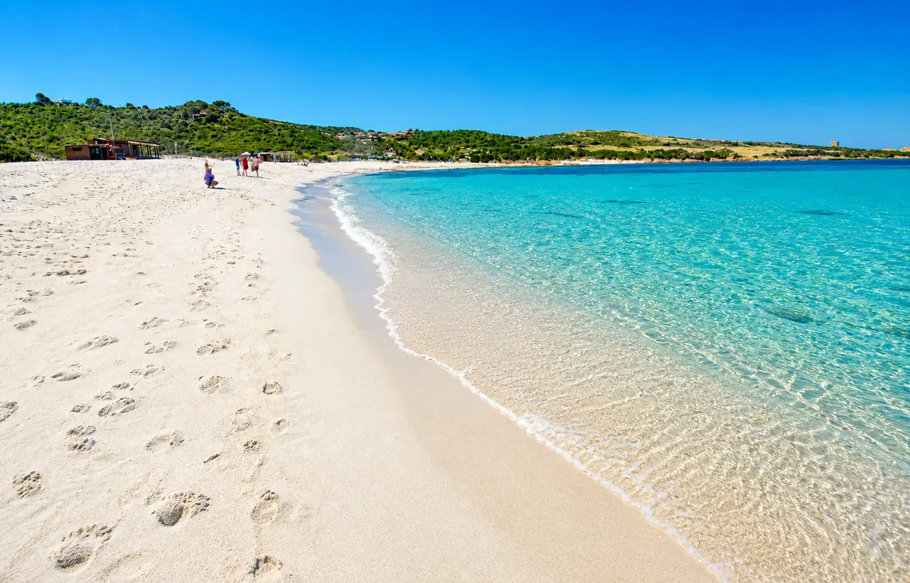 Isola Rossa, Trinità d'Agultu — spiaggia del borgo con sabbia chiara, mare turchese e costa verde sullo sfondo
